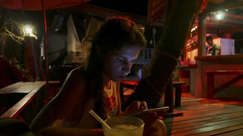 Young woman using mobile phone while sitting on chair at sidewalk cafe