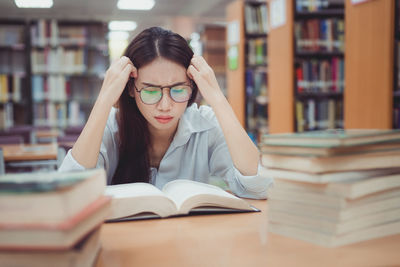 Young woman reading book while sitting in library