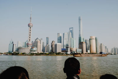 People looking at city skyline by river against clear sky