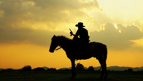Silhouette man riding horse on field against sky during sunset