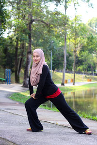 Portrait of mid adult woman wearing hijab while exercising by lake at park