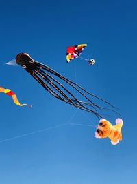 Low angle view of kites flying in clear blue sky