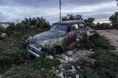 Abandoned car on landscape against sky