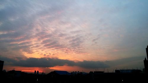 Silhouette city against dramatic sky during sunset