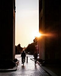 Silhouette people on street amidst buildings against sky during sunset