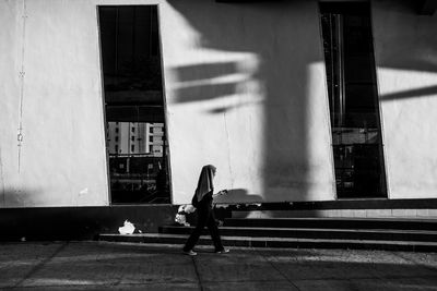 Woman walking on footpath against building in city