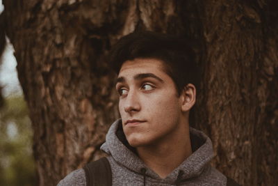 Young man looking away by trees