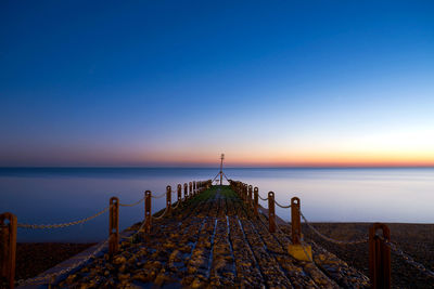 Old pier at beach against clear blue sky at sunset