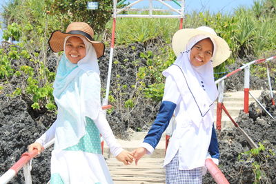 Portrait of friends wearing hijabs and hats standing at beach