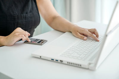 Woman is sitting at laptop and doing calculations on calculator. hands, calculator, laptop close-up