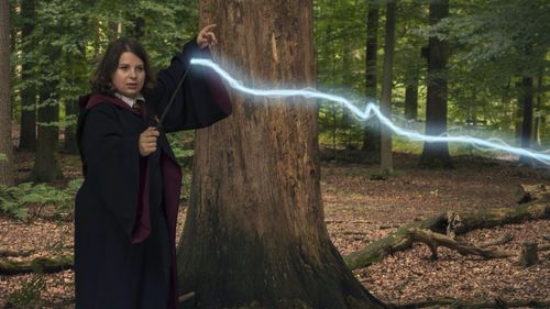 Teenage girl holding magic wand while standing by tree at forest