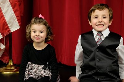 Smiling boy and girl making a face while standing against curtain