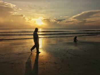 Silhouette men on beach against sky during sunset