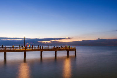 People on pier in calm sea at dusk