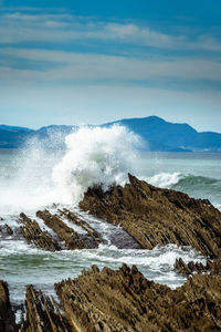 Waves splashing on rocks at shore against sky