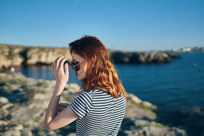 Woman photographing with arms raised standing against sky