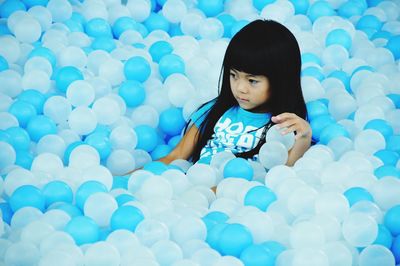 Cute girl looking away while sitting amidst blue and white helium balloons