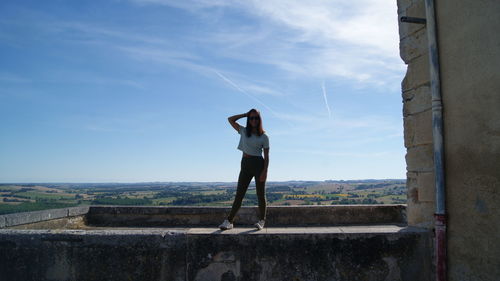 Full length of carefree woman standing on retaining wall against sky