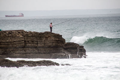 Man fishing while standing on rock by sea