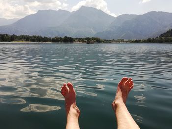 Low section of person with feet up lake against mountains