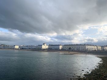 View of buildings by river against cloudy sky