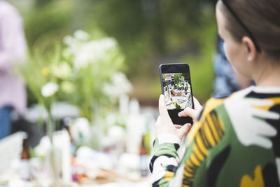 Cropped image of woman photographing dining table through mobile phone in backyard