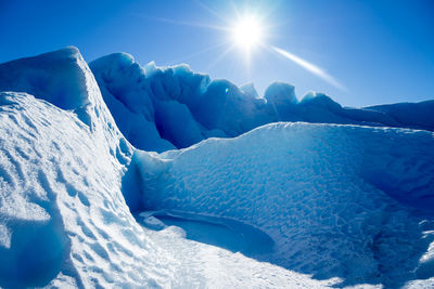 Scenic view of snowcapped mountains against blue sky on sunny day