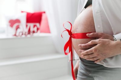 Midsection of pregnant woman with tied ribbon on belly at home