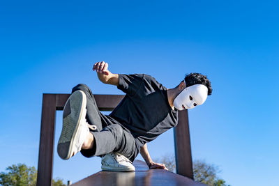 Low angle view of man sitting against blue sky
