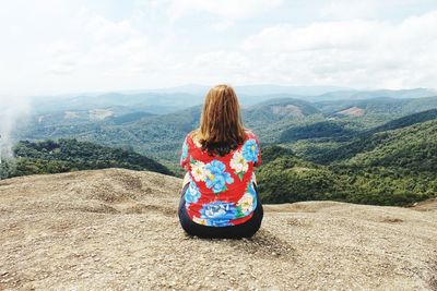 Rear view of woman sitting on mountain against sky