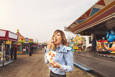 Portrait of a smiling young woman in amusement park against sky