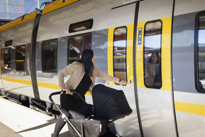 Mid adult woman at train station with pram opening train door