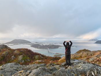 Rear view of man standing on rock against sky