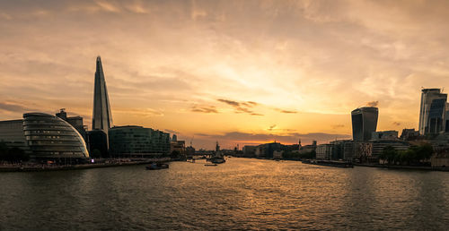 Scenic view of river by buildings against sky during sunset