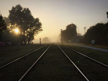 Railroad tracks amidst trees against sky during sunset