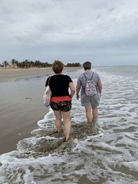 Rear view of people on beach against sky