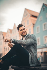 Portrait of young man sitting against building in city