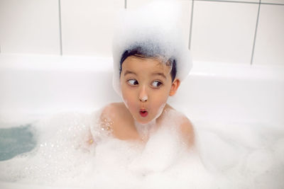 Boy with big eyes a caucasian child bathes in a white bath with foam