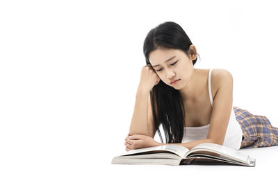 Young woman sitting on book against white background