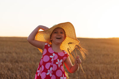 Adorable little girl in a straw hat pink summer dress in wheat field. child with long hair on sunset