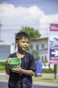 Wet boy holding bucket while standing on road