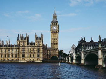 Arch bridge over river by buildings against sky in city