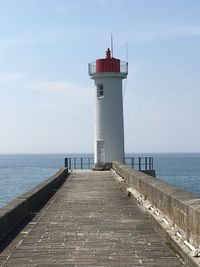 Lighthouse on pier by sea against sky