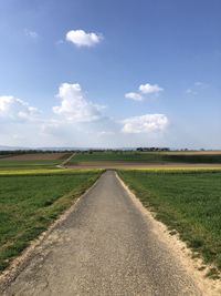 Empty road amidst field against sky
