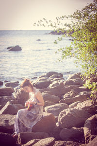 Man sitting on rock at beach against sky