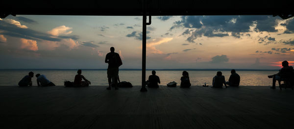 Silhouette people on sea against sky during sunset