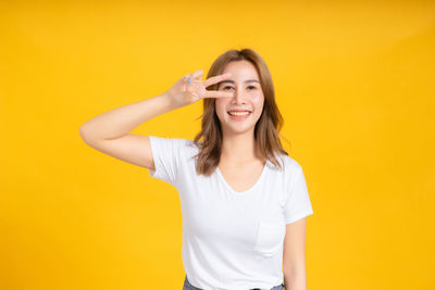 Portrait of smiling young woman against yellow background