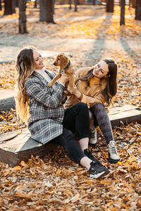 Two happy female friends girls having fun with cute cocker spaniel puppy in autumn park. two