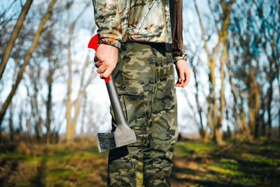 Person in camouflage clothing holding axe in the forest