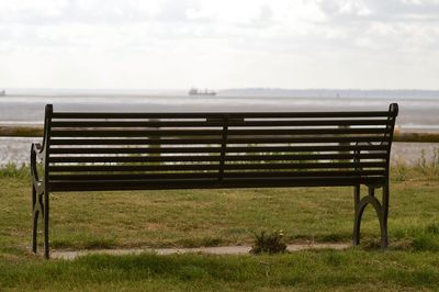 Empty bench on grass by sea against sky